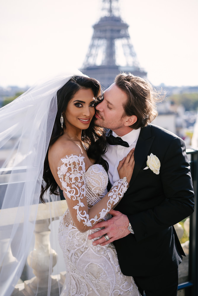 Groom kissing bride on cheek on Parisian rooftop during their elopement